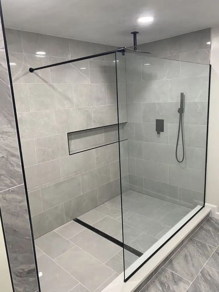 Walk-in shower with large gray porcelain tile, fixed glass panel, linear drain, long niche and matte black fixtures, Northeast Ohio