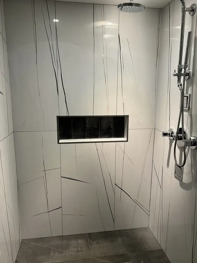 White porcelain slab shower walls with black veining, niche and chrome rain head with body sprays, Northeast Ohio