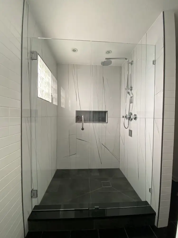 Walk-in shower with white large-format porcelain, frameless glass doors, black quartz curb and rain shower, Northeast Ohio