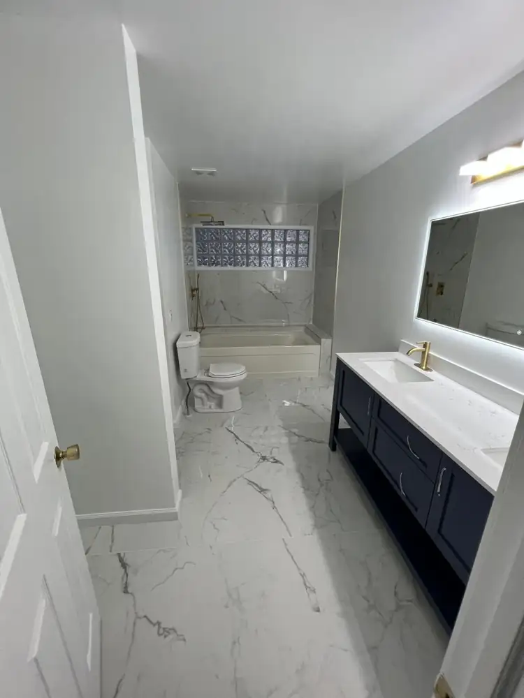 Primary bathroom with large white marble-look porcelain floor, navy double vanity and backlit mirror, Northeast Ohio