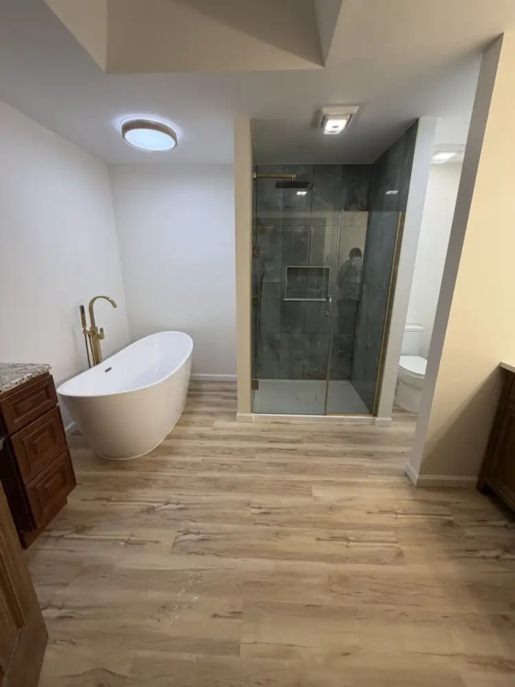 Another view: Freestanding tub with brushed gold floor-mount filler, onyx-look porcelain shower with gold trim and plank flooring, North Royalton, Ohio