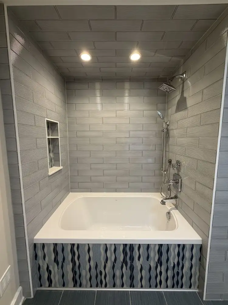 Soaking tub with textured gray tile walls and ceiling and blue wave mosaic tub front, Rocky River, Ohio