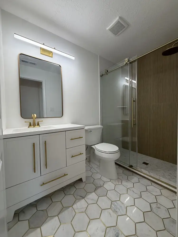 Bathroom with walk-in shower, fluted wood-look tile wall, sliding glass door, brushed gold fixtures and marble hex floor with brass inlay, Rocky River, Ohio