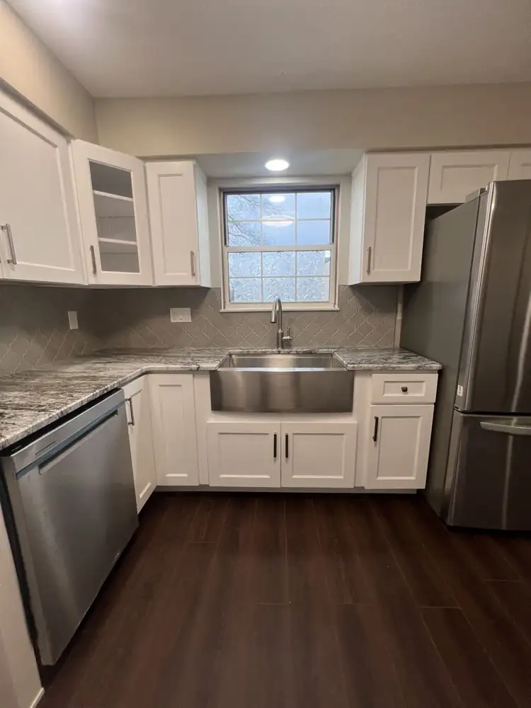 Stainless farmhouse sink under window with granite counters and arabesque backsplash