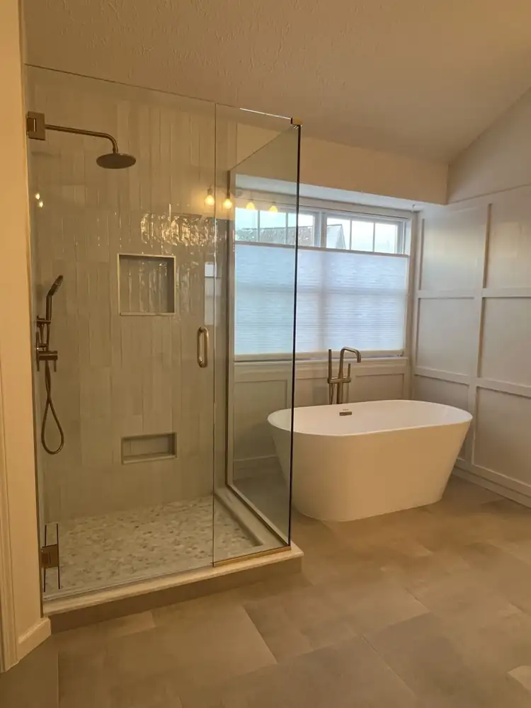 Frameless glass shower with glazed vertical tile and brushed gold fixtures beside a freestanding tub, Twinsburg