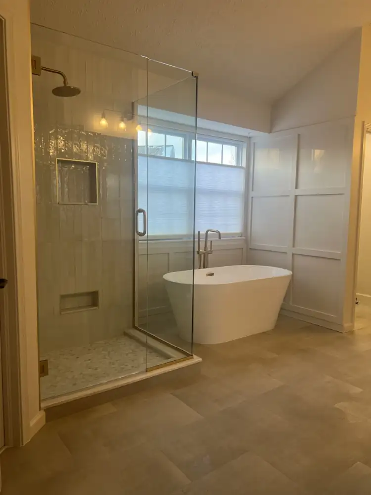 Another view: Frameless glass shower with glazed vertical tile and brushed gold fixtures beside a freestanding tub and board-and-batten wall, Twinsburg, Ohio