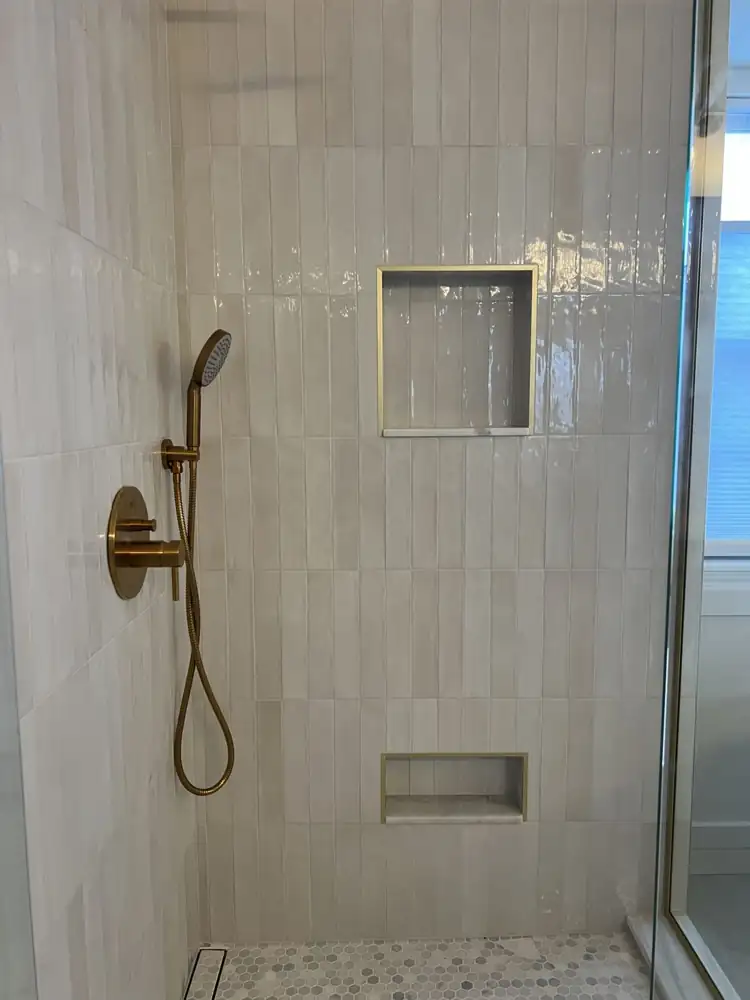 Another view: Frameless glass shower with glazed vertical tile and brushed gold fixtures beside a freestanding tub and board-and-batten wall, Twinsburg, Ohio