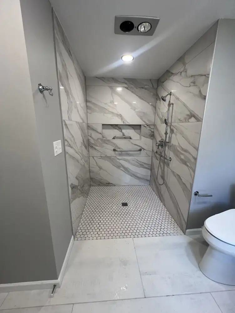Another view: Curbless walk-in shower with large-format marble-look porcelain, penny tile floor, grab bars and slide-bar handheld, Westlake, Ohio